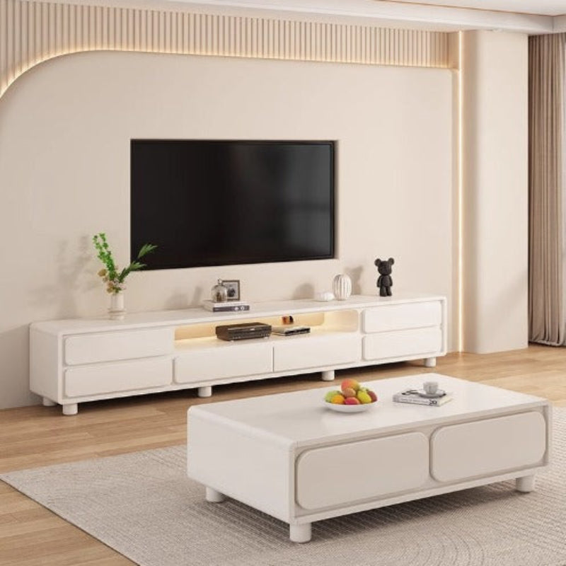 A modern white TV console with a flat-screen TV on top, placed in a living room setting with decorative items and a coffee table below.